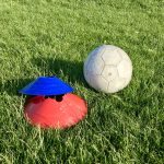 A football and some coaching space markers on the grass